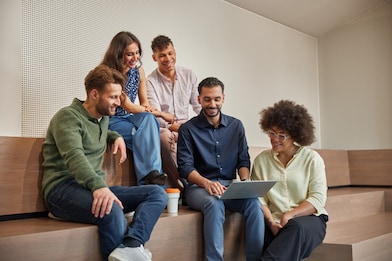 Een groep grads (2 vrouwen en 2 mannen) zitten rondom hun manager. Ze kijken glimlachend naar hun scherm