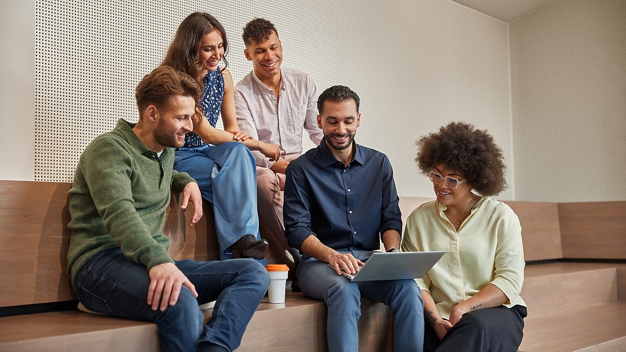Een groep graduates (2 vrouwen, 2 mannen) zitten naast hun manager (man) en kijken naar zijn scherm