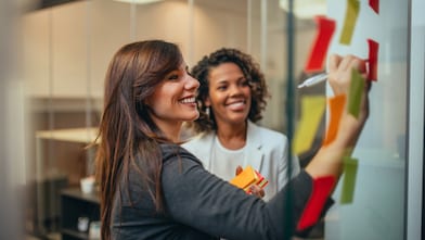 Twee medewerkers schrijven op een glazen bord.