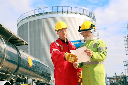 Een operator in rode overall en met gele valhelm bespreekt zaken met een collega