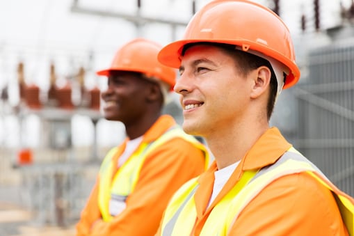 Twee medewerkers in oranje vest en met oranje valhelm op kijken naar links.