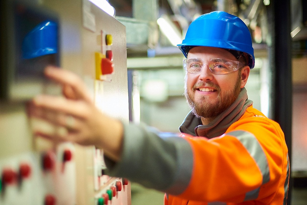 Een elektrotechnisch ingenieur lacht naar de camera terwijl hij op een knop op een bedieningspaneel drukt.