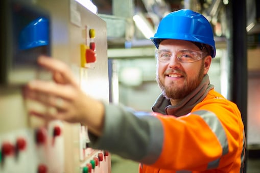 Een elektrotechnisch ingenieur lacht naar de camera terwijl hij op een knop op een bedieningspaneel drukt.