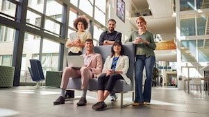 Vijf graduates staan in de gang van het kantoor gebouw en lachen naar de camera