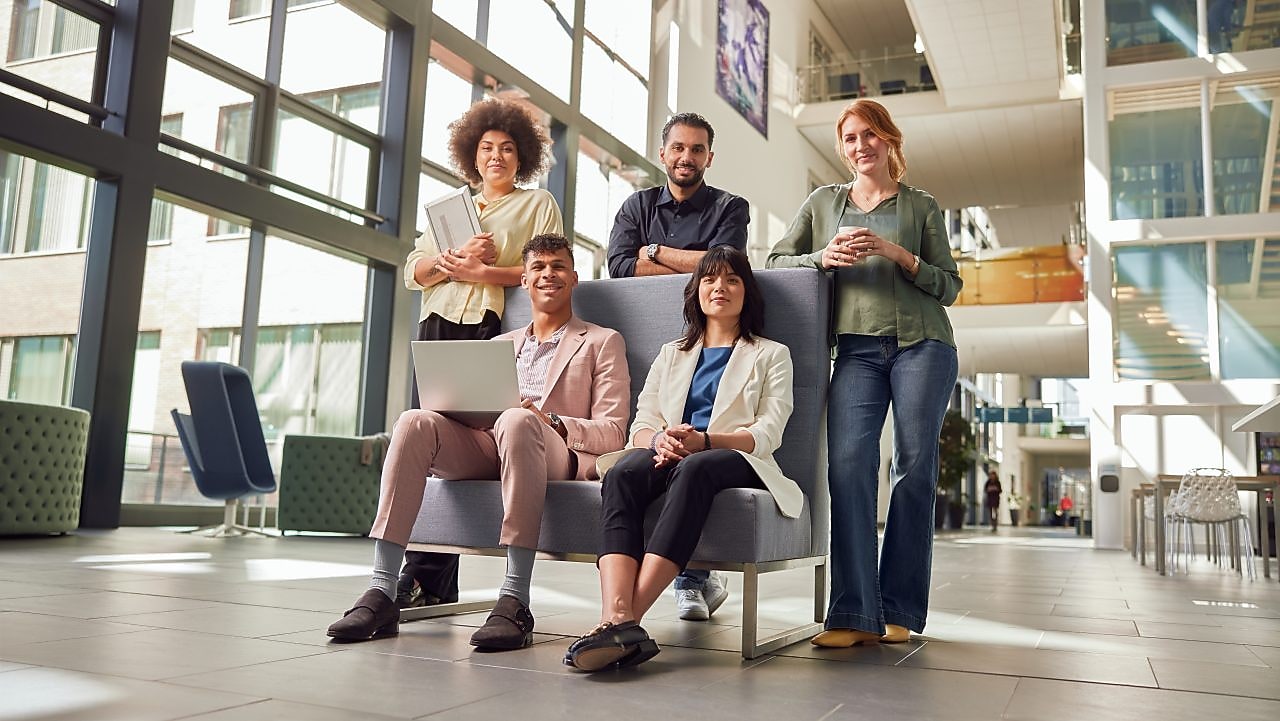 Vijf graduates staan in de gang van het kantoor gebouw en lachen naar de camera