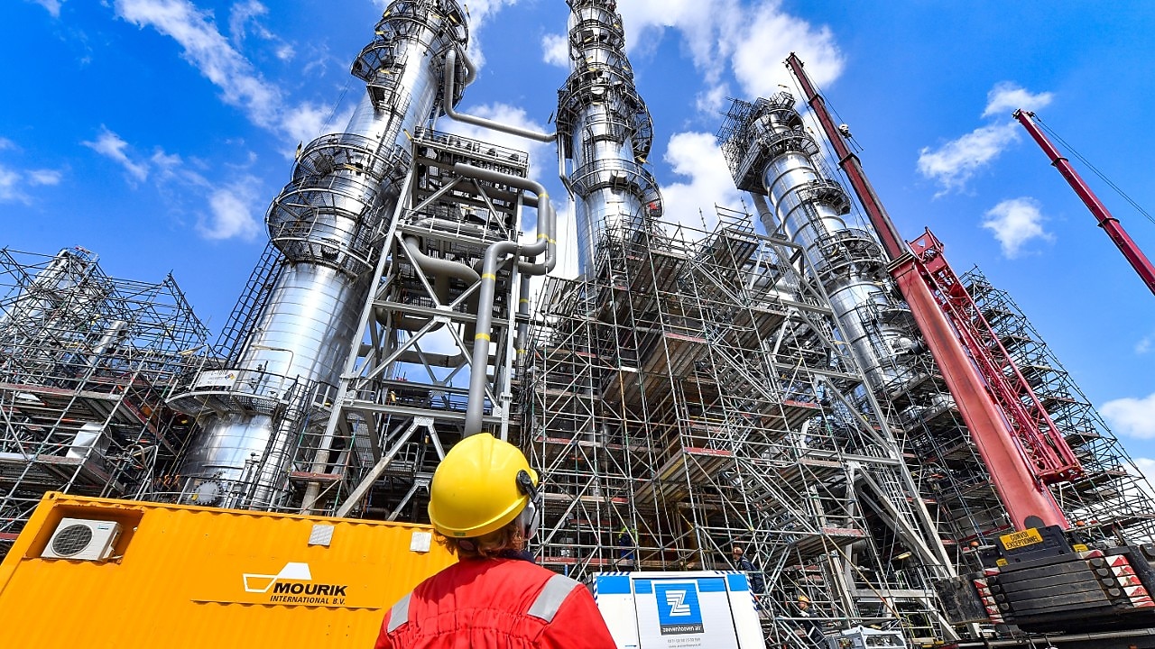 Een medewerker met helm en beschermend pak kijkt omhoog naar een van de fabrieken op Shell Chemicals Park Moerdijk