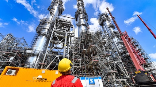 Een medewerker met helm en beschermend pak kijkt omhoog naar een van de fabrieken op Shell Chemicals Park Moerdijk