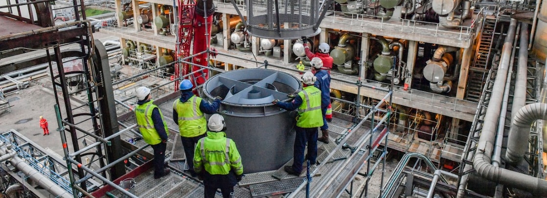 Onderhoudswerk op Shell Energy and Chemicals Park Rotterdam (Pernis). The photo shows workers in protective and reflective clothes hoisting in an element into a factory.