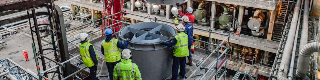 Onderhoudswerk op Shell Energy and Chemicals Park Rotterdam (Pernis). The photo shows workers in protective and reflective clothes hoisting in an element into a factory.
