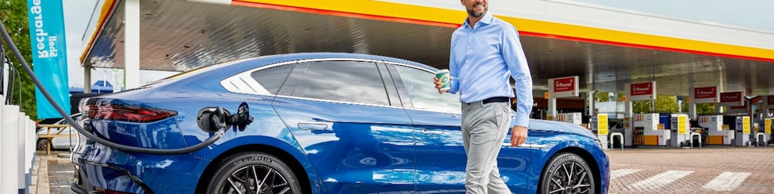 Een man loopt naar zijn elektrische auto die bij een Shell-station aan de snellader hangt