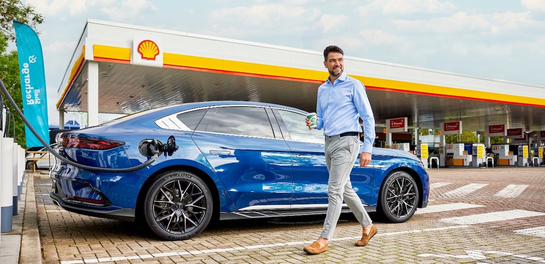Een man loopt naar zijn elektrische auto die bij een Shell-station aan de snellader hangt