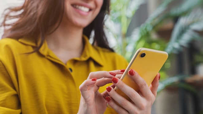 Een vrouw met gele blouse en een mobiel in haar hand