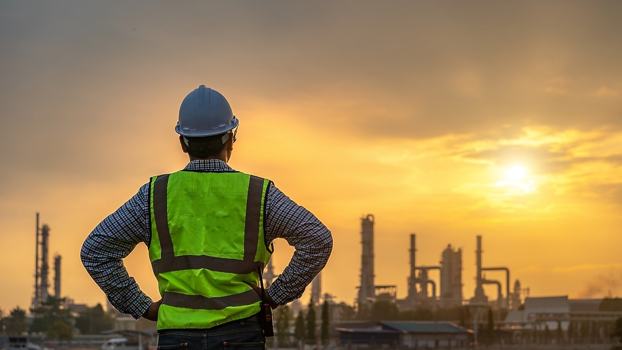 Een man kijkt naar de zonsondergang boven een fabriek