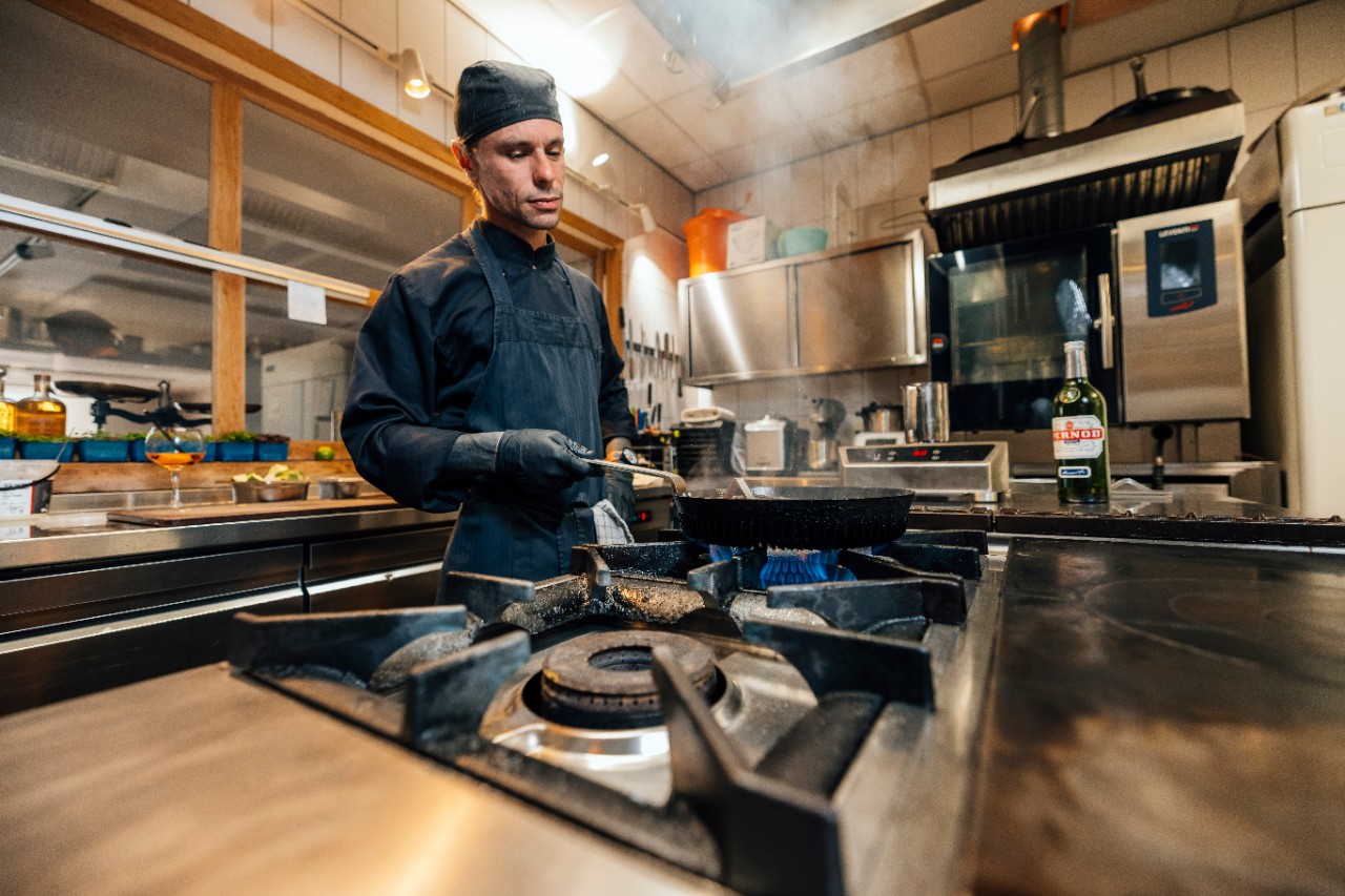 Een professionele kok in een Nederlandse keuken gebruikt de Effium-pan op het gasfornuis.