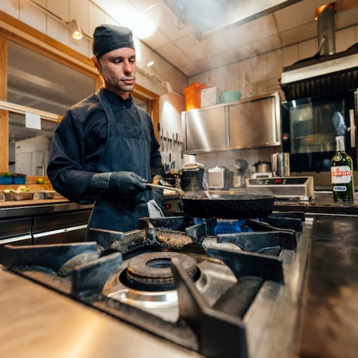 Een professionele kok in een Nederlandse keuken gebruikt de Effium-pan op het gasfornuis.