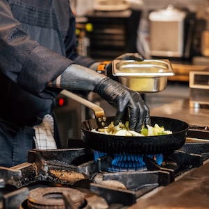 Close-up van de Effium-pan in actie. De kok husselt de groenten en andere ingrediënten in de pan die op het gasfornuis staat.