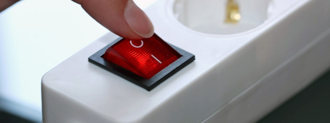 Vinger op de uitknop van de stopcontactdoos (Foto: AdobeStock)