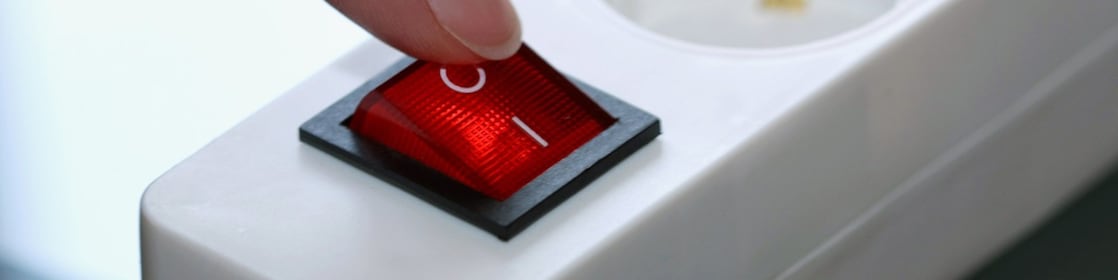 Vinger op de uitknop van de stopcontactdoos (Foto: AdobeStock)
