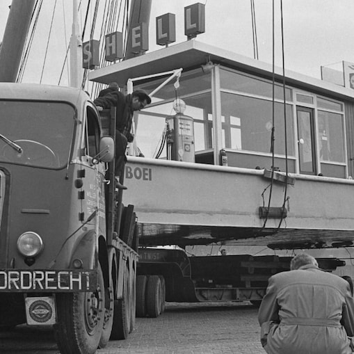 Op de foto wordt het station — „Shell Boei" geheten na uit de Amstel te zijn gehesen, op wielstellen naar het nieuwe RAI-gebouw in Amsterdam getransporteerd, waar het op de tentoonstelling Hiswa - Goed Kamp zou komen te staan, 14 maart 1963 (Foto: Hugo van Gelderen/Anefo/Nationaal Archief)