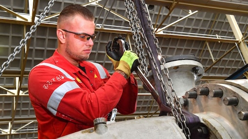 Stefan de Visser in de weer in de Centrale Werkplaats van Shell Pernis. Hij heeft kort haar, draagt een beschermbril en handschoenen. Hij heeft een grote sleutel van ongeveer een 50 centimeter groot vast waarmee hij iets aandraait op een metalen constructie (Beeld: Ernst Bode)