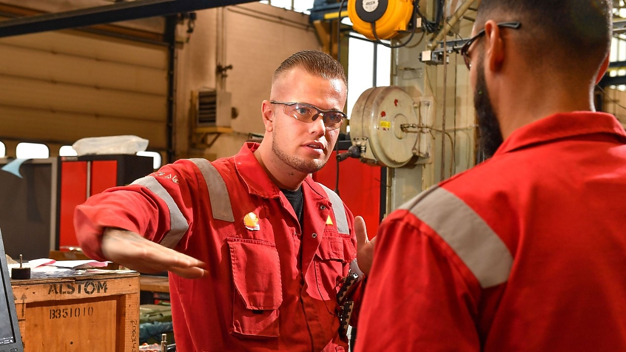 Stefan legt iets uit aan een collega. Hij gebruikt zijn rechterhand om iets aan te geven, terwijl hij oogcontact houdt met de collega die met zijn rug naar de camera staat (Beeld: Ernst Bode)