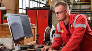 Stefan bekijkt een werkorder op een computerscherm. Hij heeft zijn handen op het toetsenbord. Op de achtergrond is de werkplaats zichtbaar (Beeld: Ernst Bode)