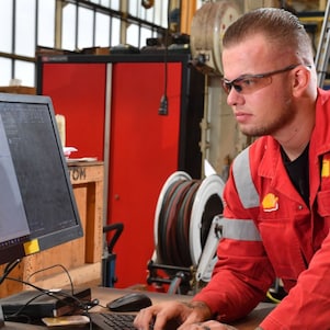 Stefan bekijkt een werkorder op een computerscherm. Hij heeft zijn handen op het toetsenbord. Op de achtergrond is de werkplaats zichtbaar (Beeld: Ernst Bode)