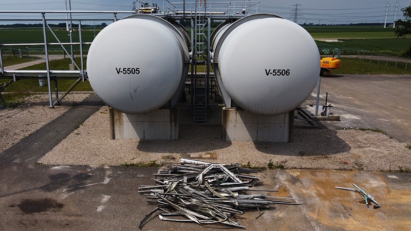 Two grey tanks still intact, with recycle metal just in front (Photo: NAM)