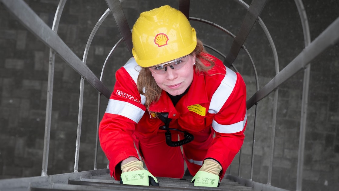 Tineke van Paassen in rode overal en met gele beschermhelm bij de Shell-fabriek in Moerdijk