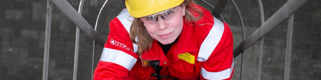 Tineke van Paassen in rode overal en met gele beschermhelm bij de Shell-fabriek in Moerdijk