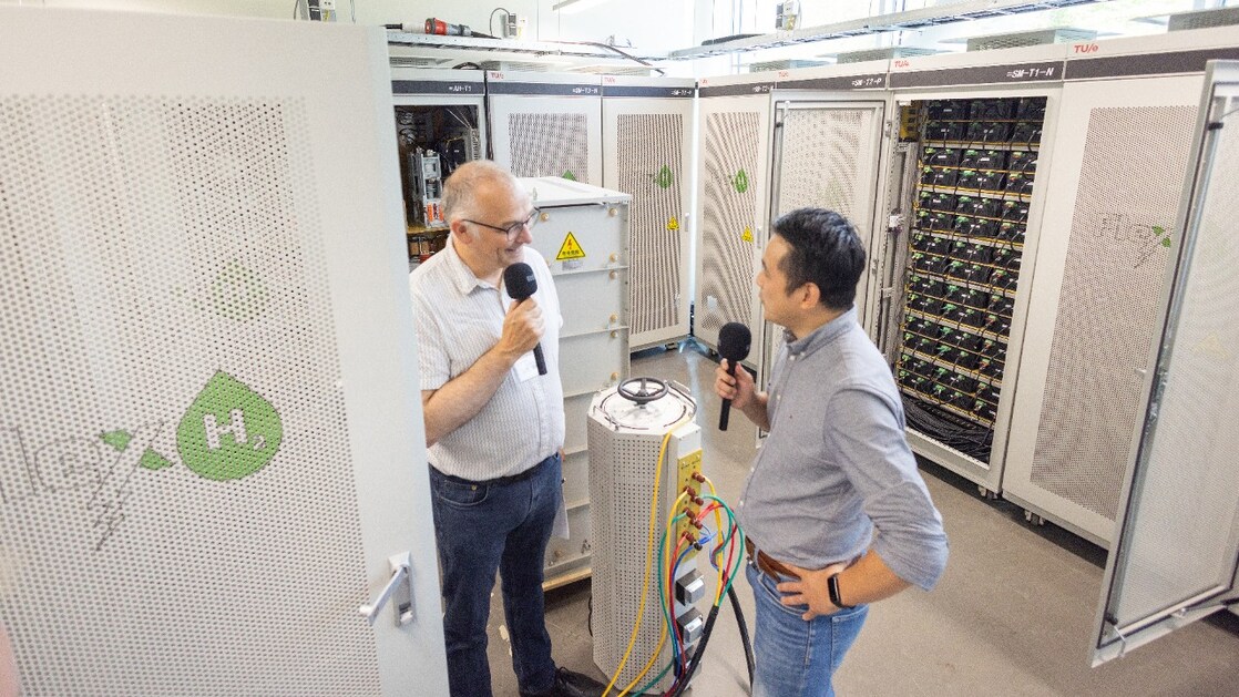 In de FlexH2-testopstelling bij Differ op het terrein van de TU Eindhoven. Yin Sun (rechts) in gesprek met een bezoekende podcastpresentator (Foto: Joep van Drunen)