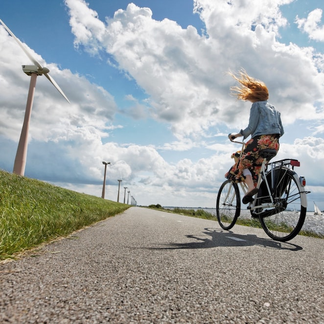 Een vrouw op de fiets op een dijk met windturbines (Foto: Getty Images)