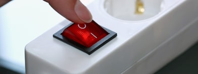 Vinger op de uitknop van de stopcontactdoos (Foto: AdobeStock)