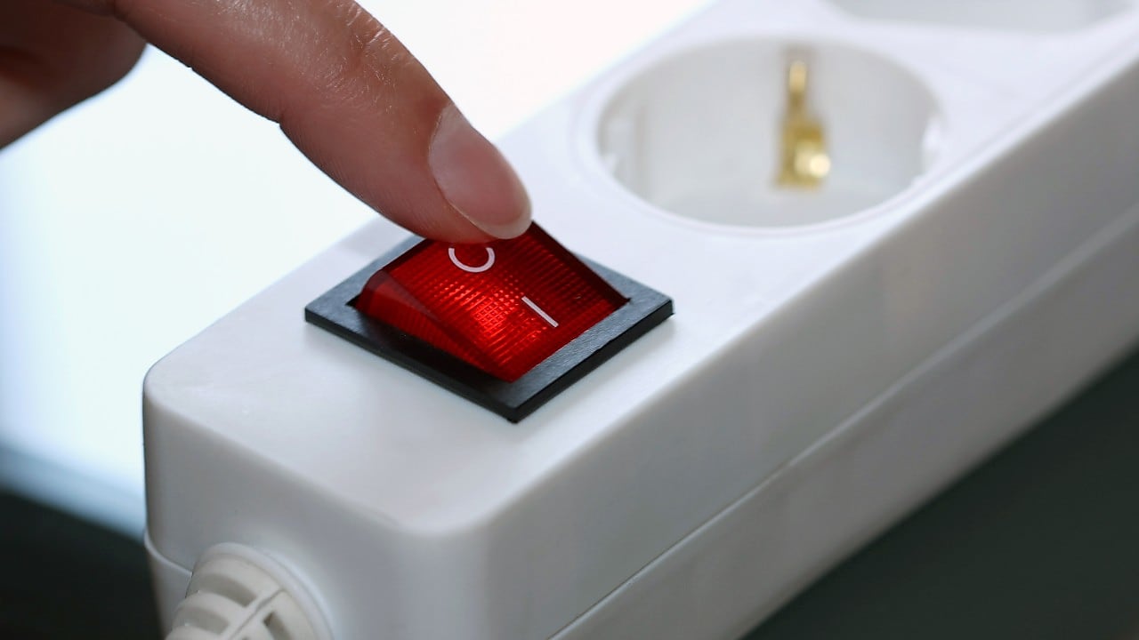 Vinger op de uitknop van de stopcontactdoos (Foto: AdobeStock)