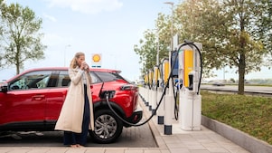 Een dame bij haar elektrische auto die aan de laadpaal hangt (Foto: Shell Recharge)