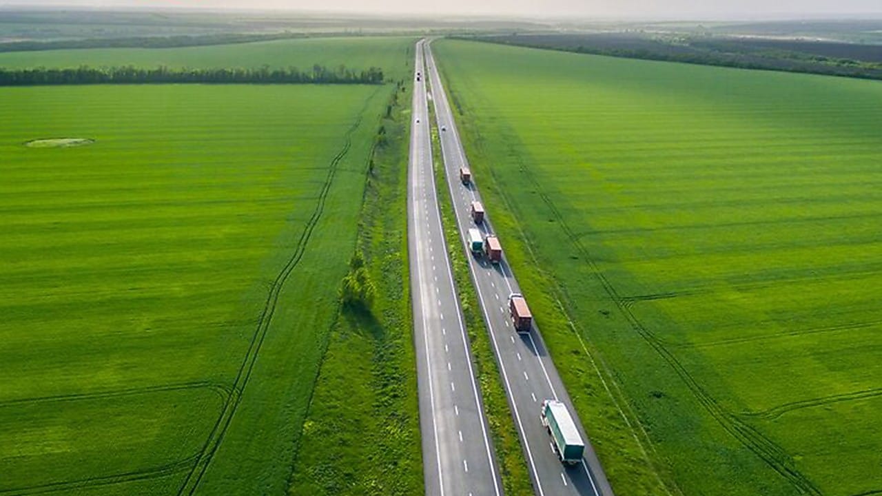 Trucks on a highway in a green field landscape