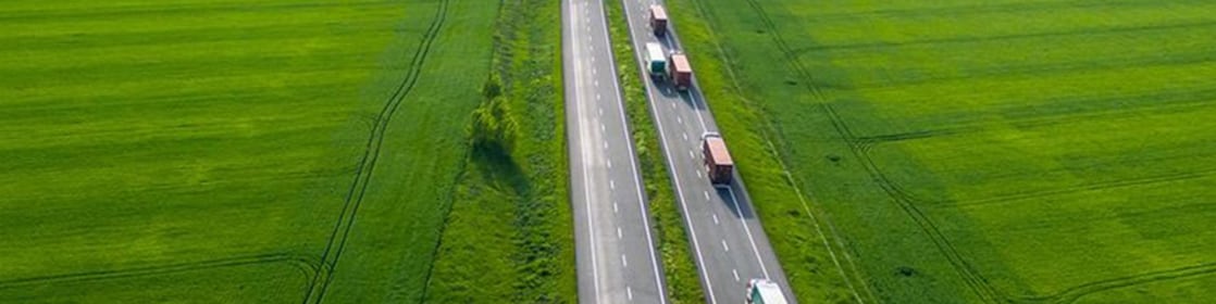 Trucks on a highway in a green field landscape