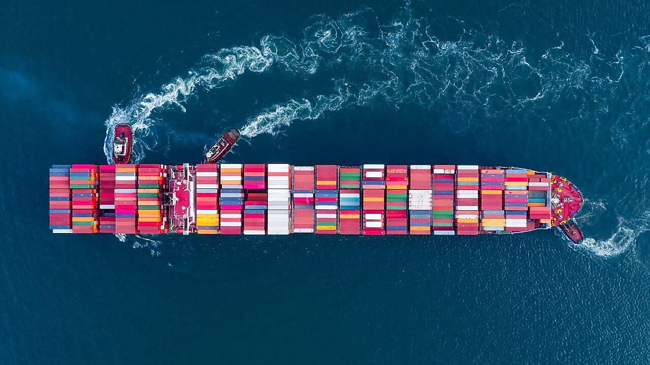 A container ship seen from above, pushed by tug boats.