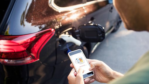 Een man bekijkt op zijn mobiel de Shell App terwijl zijn wagen aan de elektrische lader hangt