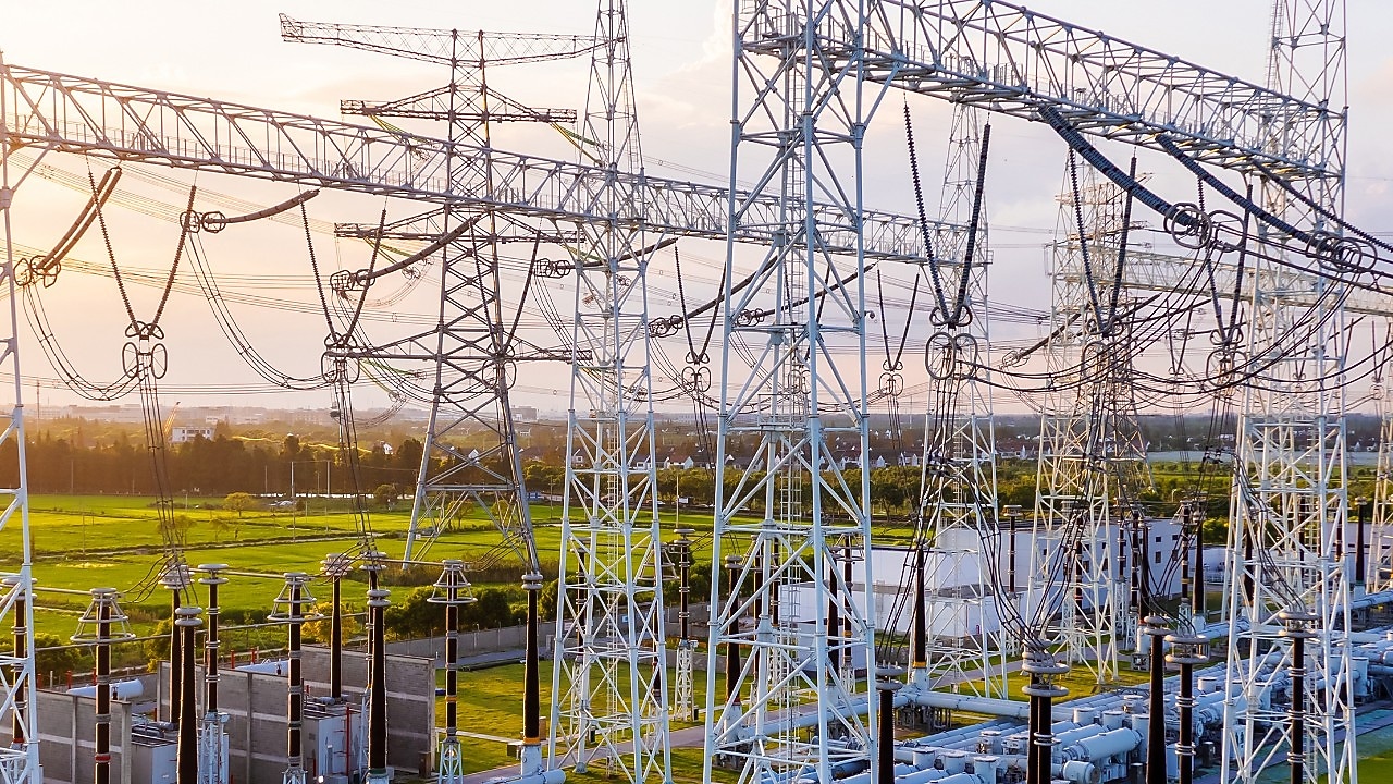 Transformatorstation met onderling verbonden hoogspanningsleidingen en apparatuur bij zonsondergang.