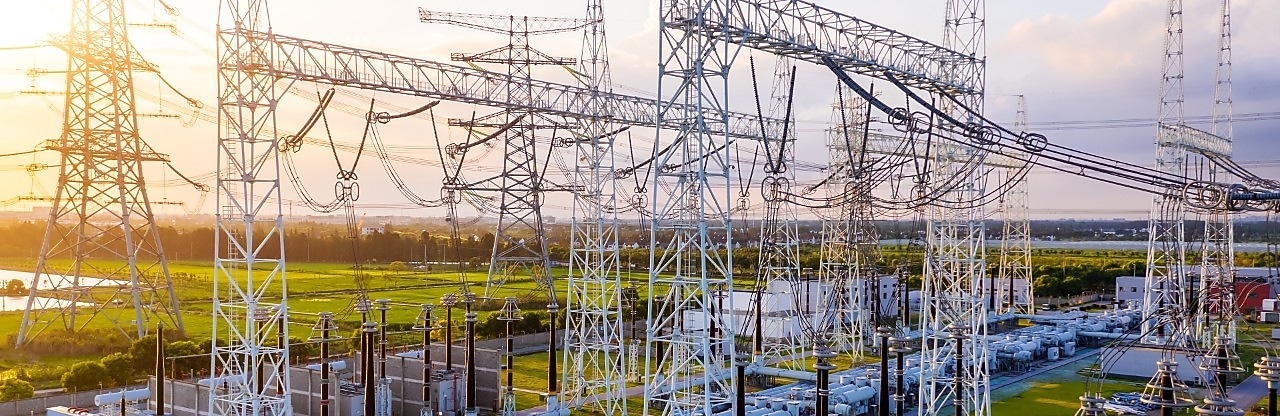Transformatorstation met onderling verbonden hoogspanningsleidingen en apparatuur bij zonsondergang.