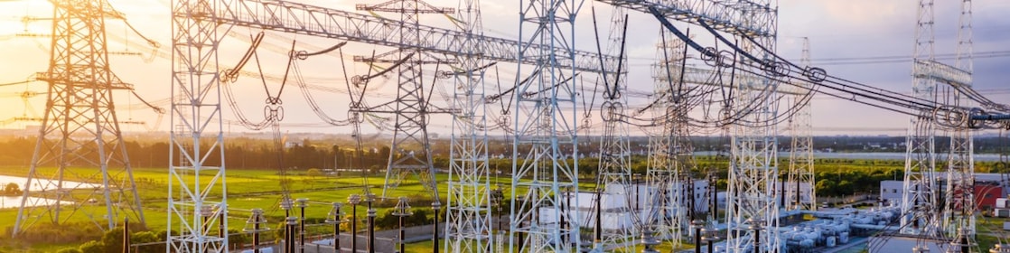 Transformatorstation met onderling verbonden hoogspanningsleidingen en apparatuur bij zonsondergang.