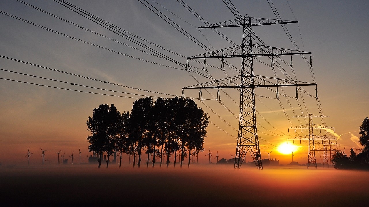 Hoogspanningskabels in een landschap tijdens zonsondergang.