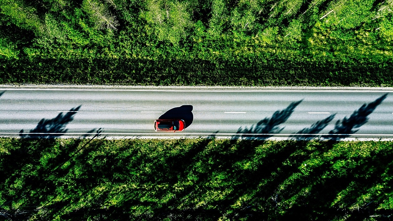 Een rode wagen op een weg door het bos, gezien van bovenaf