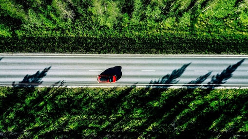 Een rode wagen op een weg door het bos, gezien van bovenaf