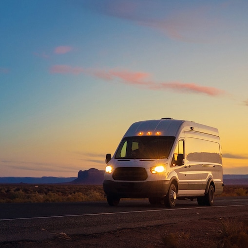 Een wit bestelbusje op de weg met ondergaande zon