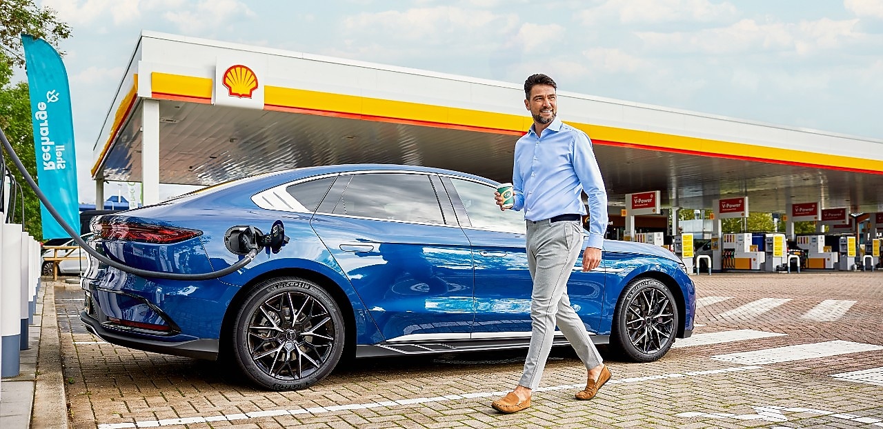 Een blauwe elektrische auto aan de Shell Recharge-laadpaal en een man die naar zijn auto loopt.