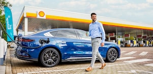 Een blauwe elektrische auto aan de Shell Recharge-laadpaal en een man die naar zijn auto loopt.