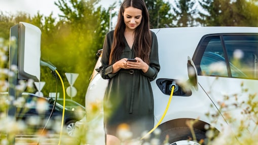 Een vrouw kijkt op haar mobiele telefoon terwijl ze haar elektrische auto laadt
