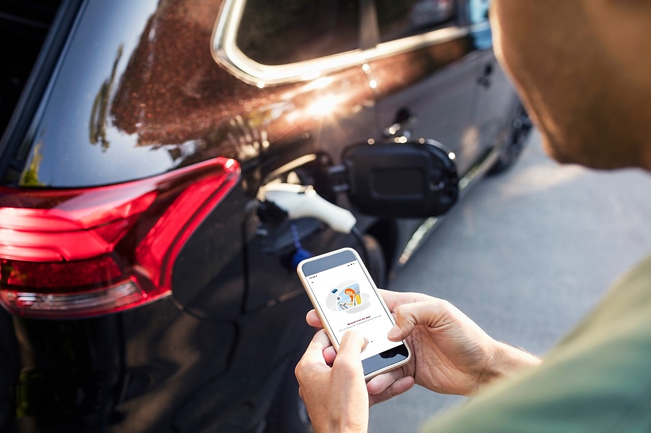 Man gebruikt zijn mobiele telefoon bij een zwarte auto.